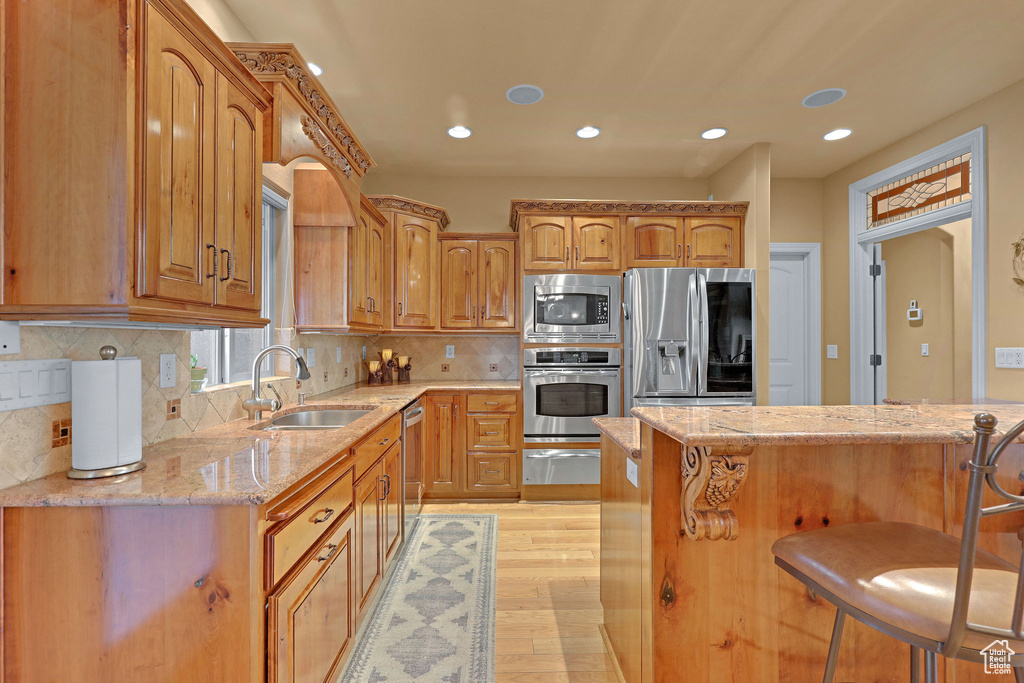 Kitchen featuring appliances with stainless steel finishes, a sink, light stone counters, a breakfast bar area, and a warming drawer