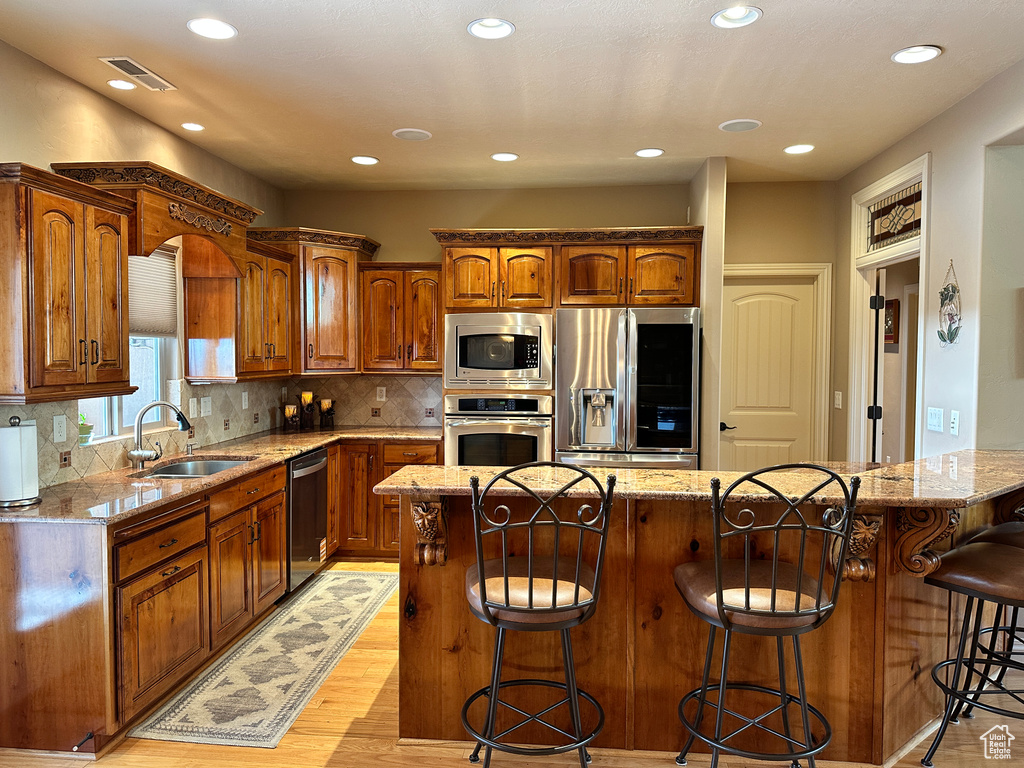 Kitchen with stainless steel appliances, a sink, a breakfast bar, light wood-type flooring, and light stone countertops