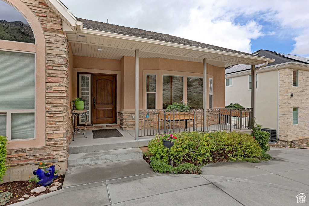 Entrance to property featuring stone siding, a porch, stucco siding, and central AC unit