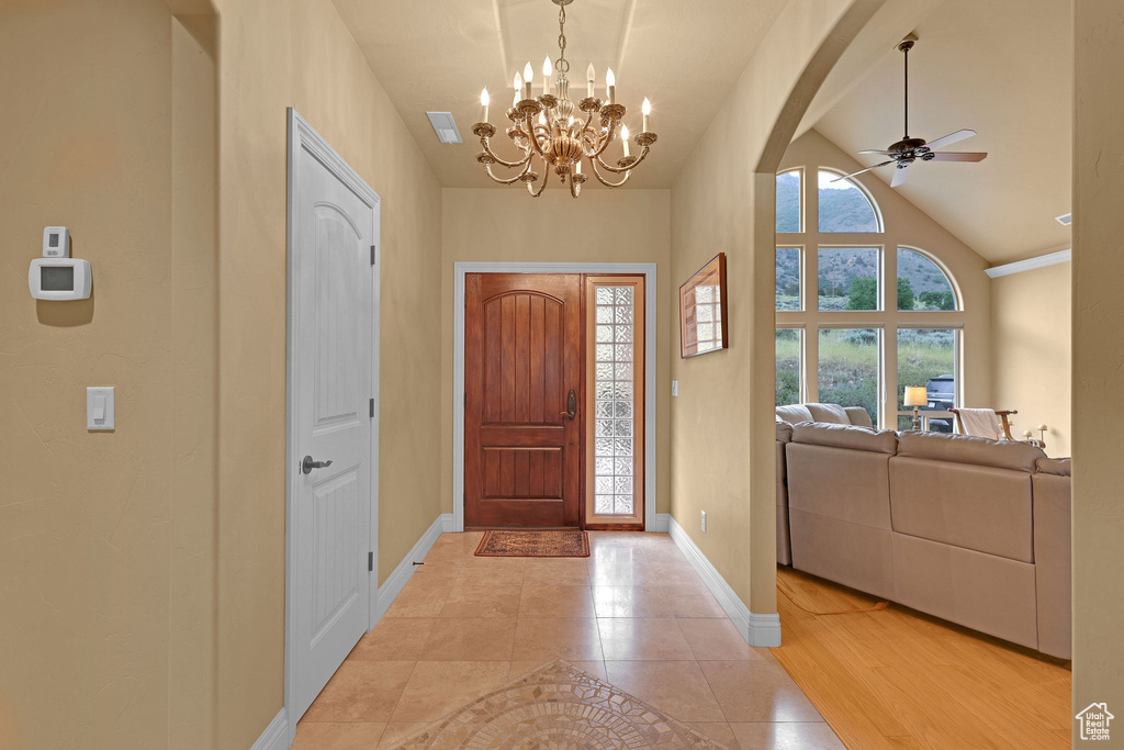 Entrance foyer with baseboards, ceiling fan, a chandelier, arched walkways, and light tile patterned floors
