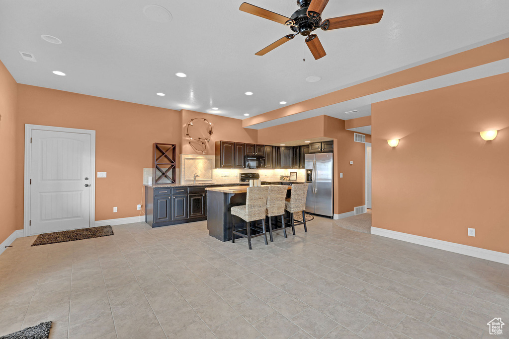 Kitchen featuring stainless steel refrigerator with ice dispenser, a kitchen bar, a center island, a ceiling fan, and baseboards