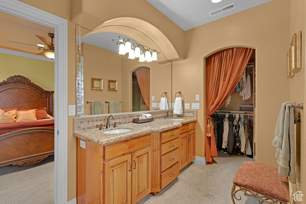 Ensuite bathroom with ceiling fan, double vanity, a walk in closet, and backsplash