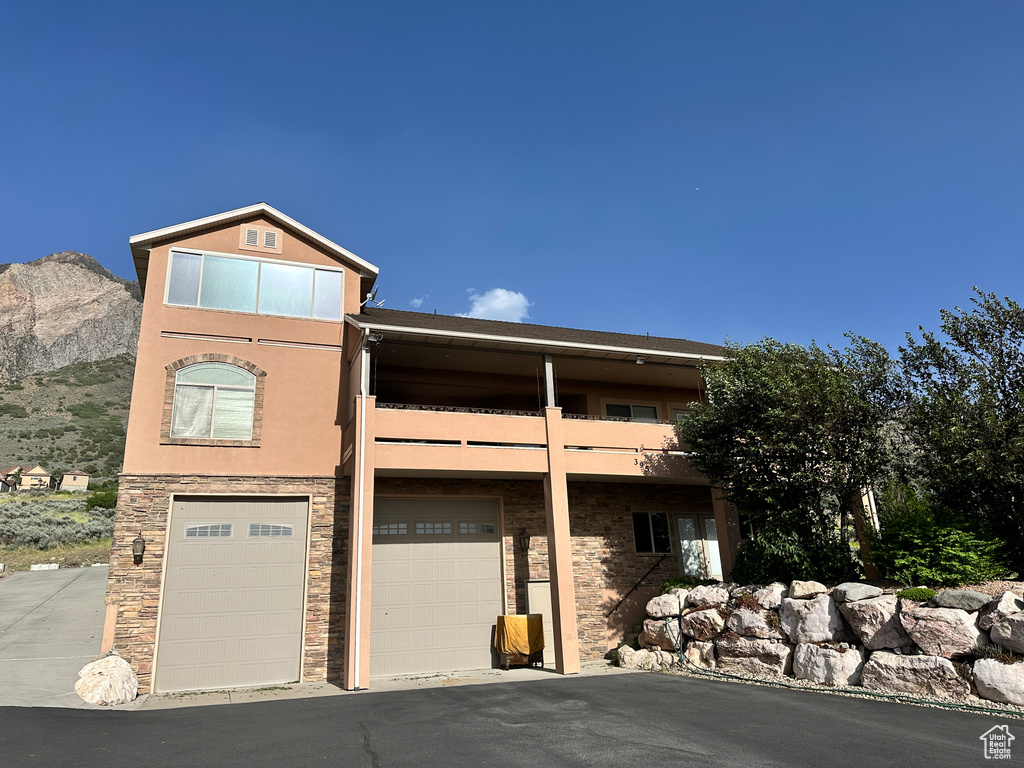View of front of property featuring an attached garage, a balcony, stone siding, stucco siding, and a mountain view