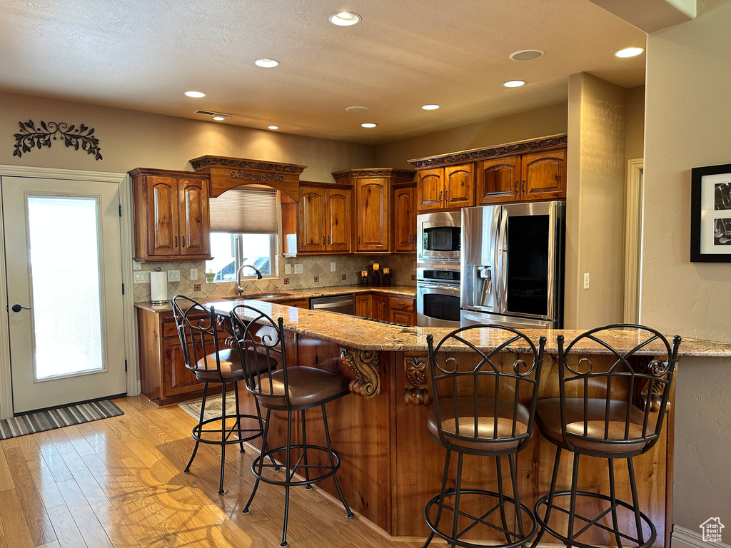 Kitchen with stainless steel appliances, a sink, light wood-type flooring, a breakfast bar, and recessed lighting