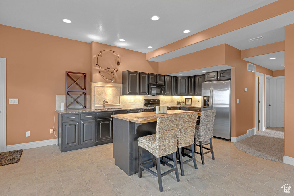 Kitchen with stainless steel fridge with ice dispenser, black microwave, baseboards, a kitchen island, and recessed lighting