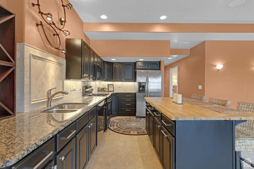 Kitchen featuring stainless steel fridge, a sink, black microwave, butcher block countertops, and a kitchen breakfast bar