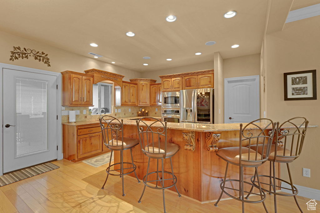 Kitchen featuring stainless steel appliances, a breakfast bar area, light wood-type flooring, brown cabinets, and recessed lighting