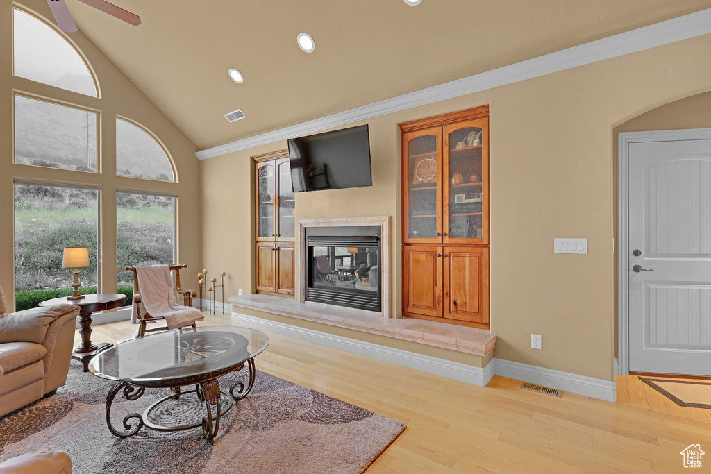 Living area with a glass covered fireplace, wood finished floors, baseboards, recessed lighting, and ornamental molding