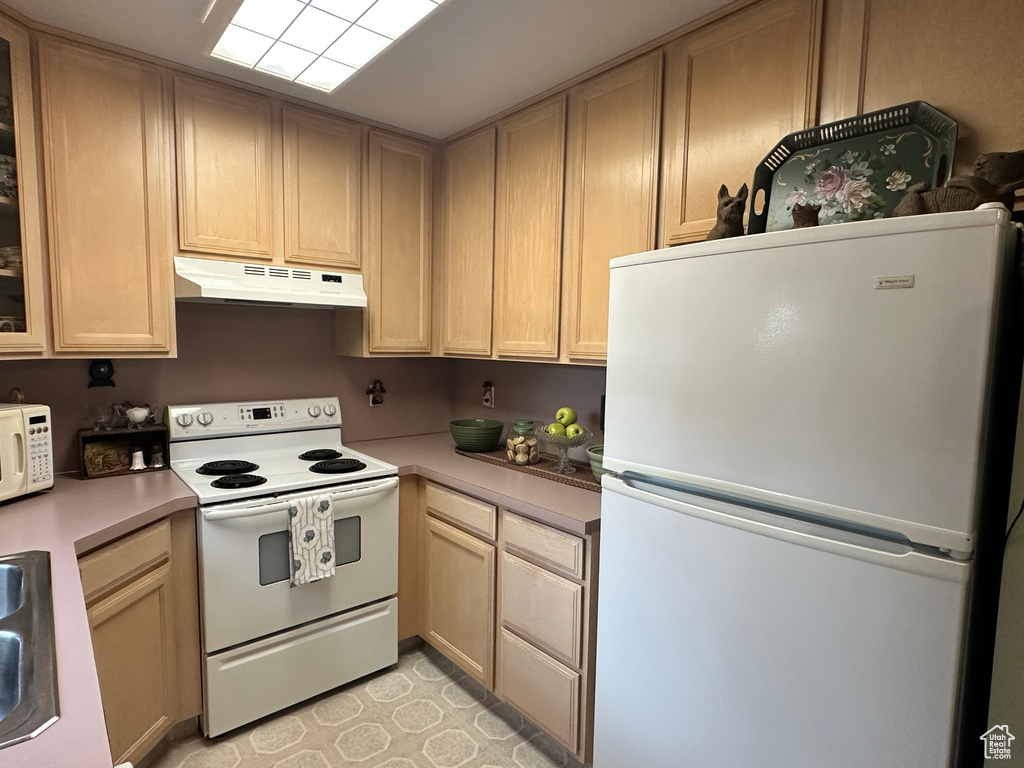 Kitchen with white appliances, under cabinet range hood, light countertops, and glass insert cabinets
