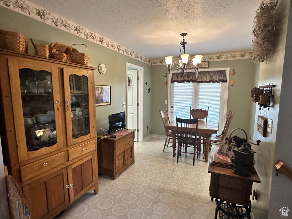 Dining room with a textured ceiling, a chandelier, light flooring, and baseboards