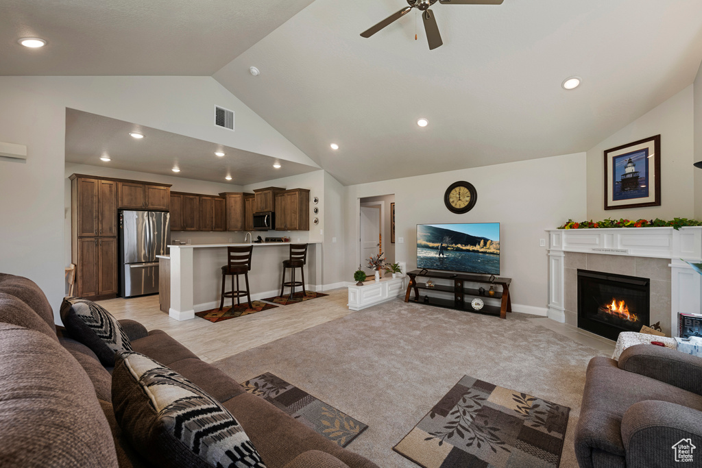 Living area with ceiling fan, a tile fireplace, recessed lighting, high vaulted ceiling, and light carpet