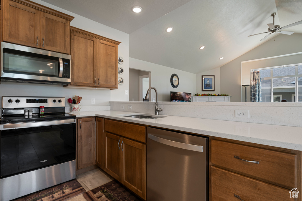 Kitchen with stainless steel appliances, a sink, vaulted ceiling, brown cabinets, and ceiling fan