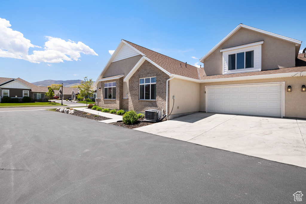 View of front facade featuring concrete driveway, stucco siding, a mountain view, an attached garage, and central air condition unit