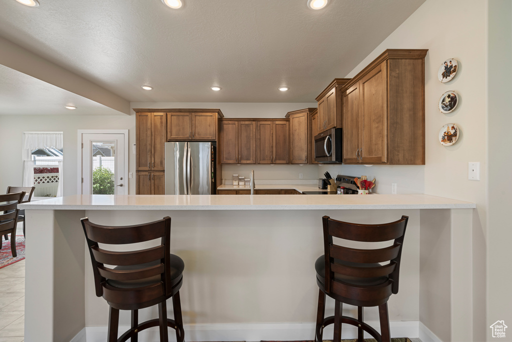 Kitchen with appliances with stainless steel finishes, a peninsula, recessed lighting, a kitchen breakfast bar, and light countertops