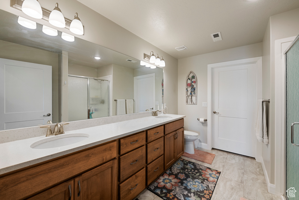 Bathroom featuring a shower stall, double vanity, toilet, and baseboards