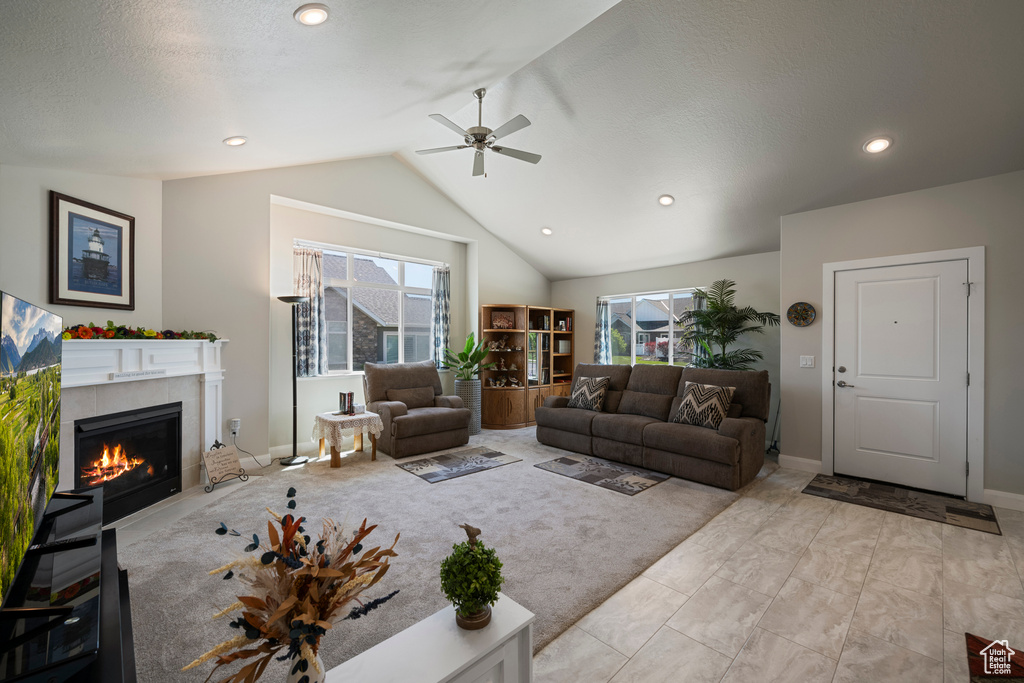 Living area with plenty of natural light, vaulted ceiling, a ceiling fan, a tiled fireplace, and baseboards