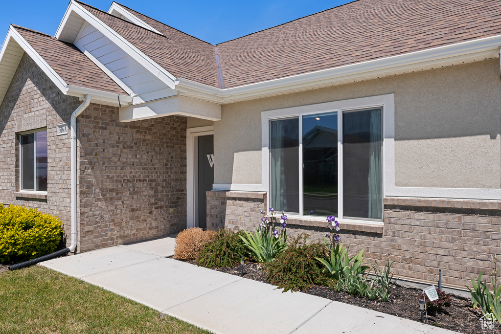 Entrance to property featuring a shingled roof, stucco siding, and brick siding