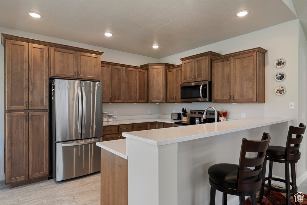 Kitchen with appliances with stainless steel finishes, a peninsula, light countertops, a breakfast bar area, and recessed lighting
