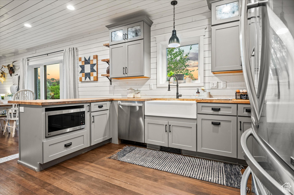 Kitchen with stainless steel appliances, gray cabinets, butcher block countertops, plenty of natural light, and wooden walls