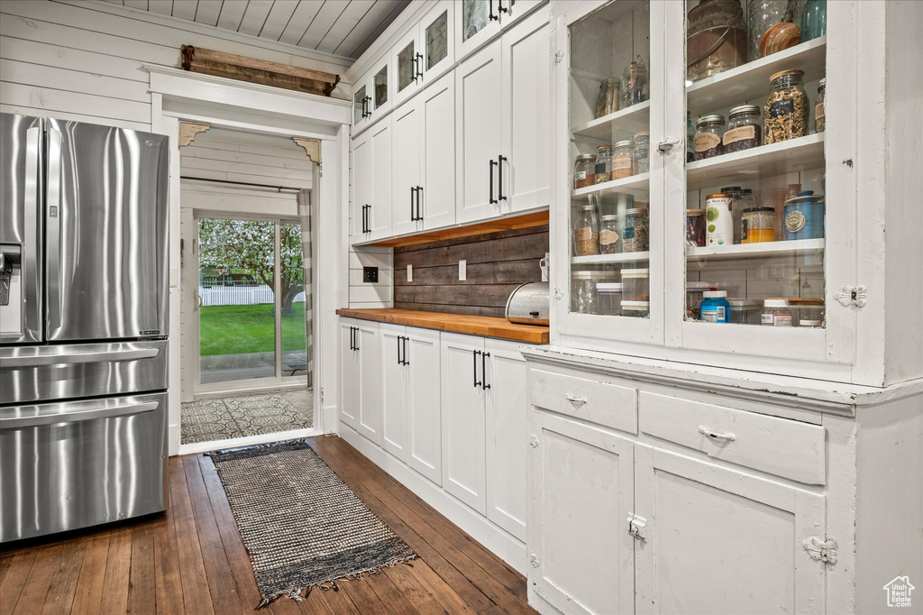 Kitchen featuring stainless steel refrigerator with ice dispenser, dark wood-style flooring, butcher block counters, white cabinetry, and backsplash