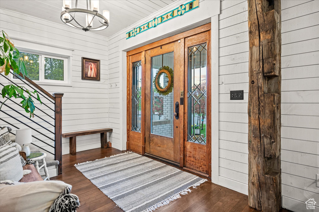 Foyer with wood finished floors, a chandelier, wood walls, and crown molding