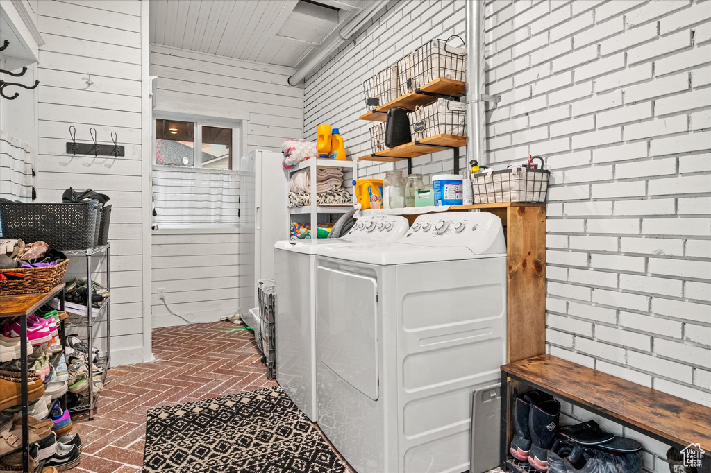 Washroom with washer and dryer, brick flooring, and wooden walls