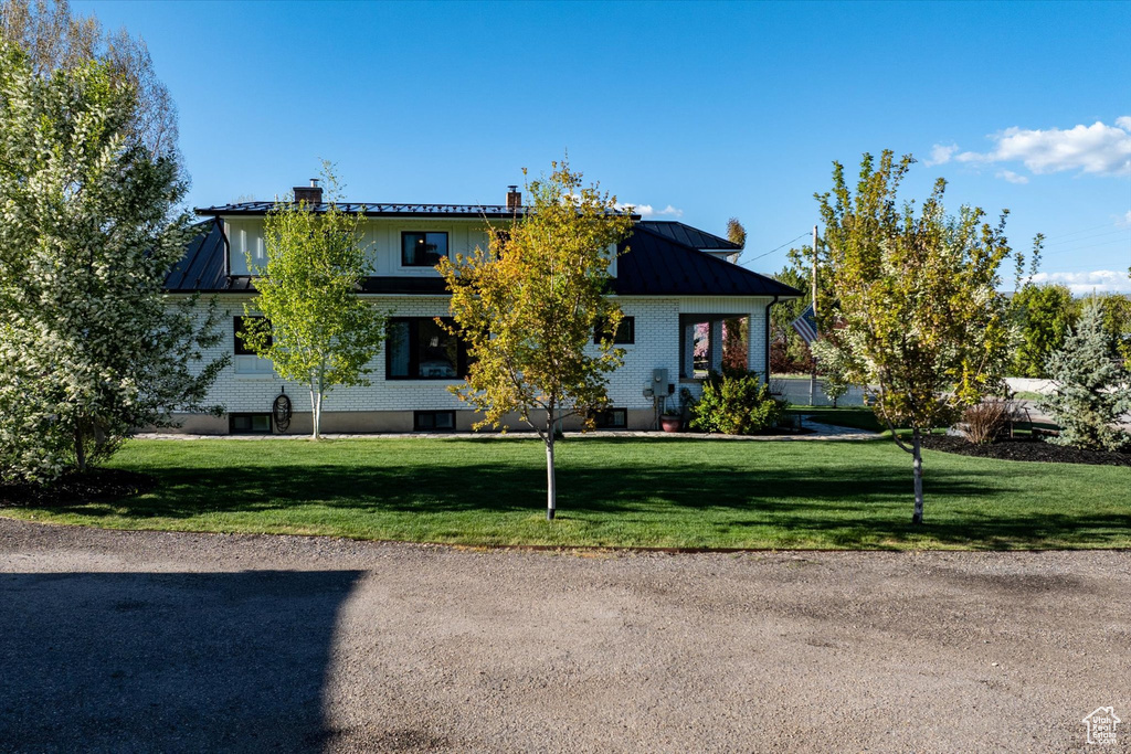 Obstructed view of property with a standing seam roof, a front yard, metal roof, and a chimney