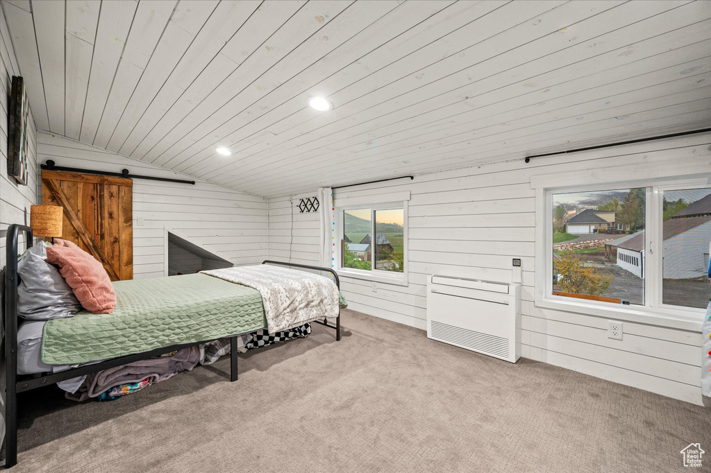 Carpeted bedroom featuring wooden ceiling, a barn door, wood walls, lofted ceiling, and multiple windows