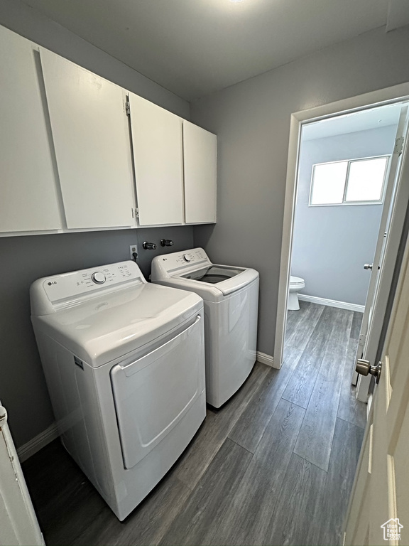 Laundry area with independent washer and dryer, cabinet space, dark wood-style flooring, and baseboards