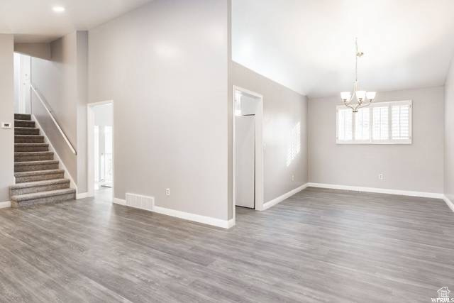 Unfurnished living room featuring a chandelier, stairs, baseboards, and wood finished floors