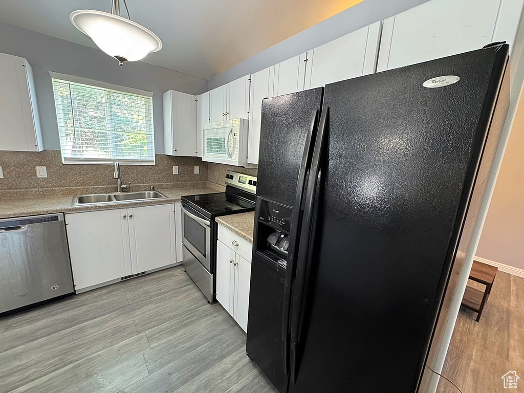 Kitchen with appliances with stainless steel finishes, a sink, light wood finished floors, tasteful backsplash, and white cabinets