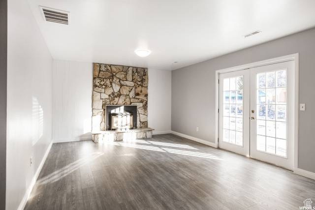 Unfurnished living room with french doors, wood finished floors, baseboards, and a stone fireplace