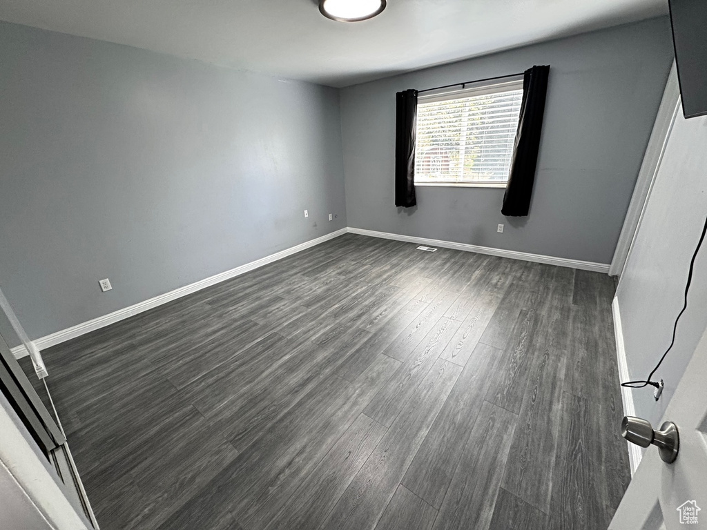 Spare room with dark wood-style flooring and baseboards