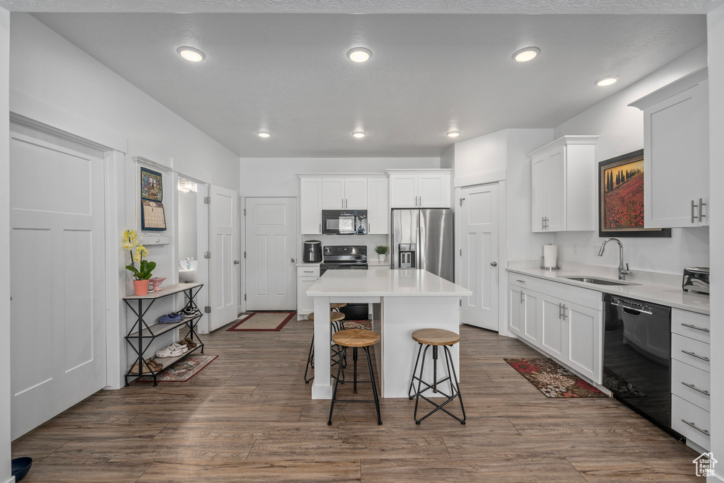 Kitchen featuring black appliances, a sink, a kitchen island, a breakfast bar area, and white cabinetry