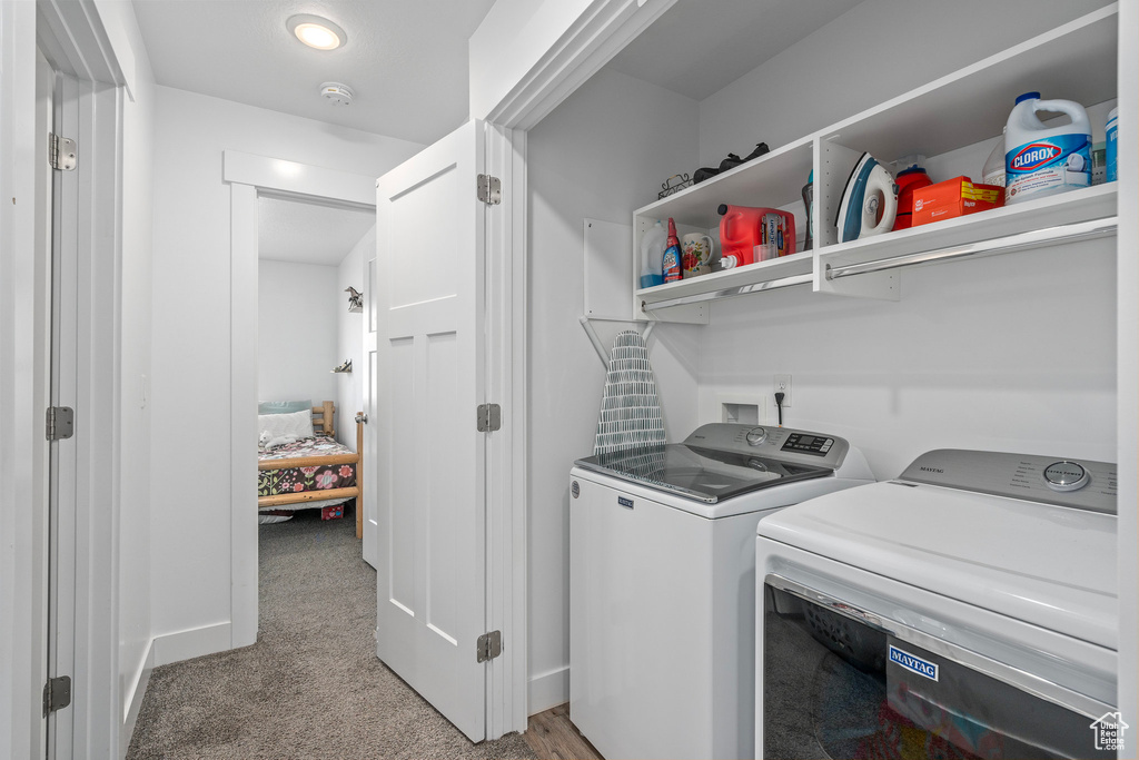 Clothes washing area with washer and dryer, light carpet, and baseboards