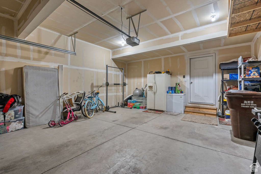Garage featuring white refrigerator with ice dispenser and a garage door opener