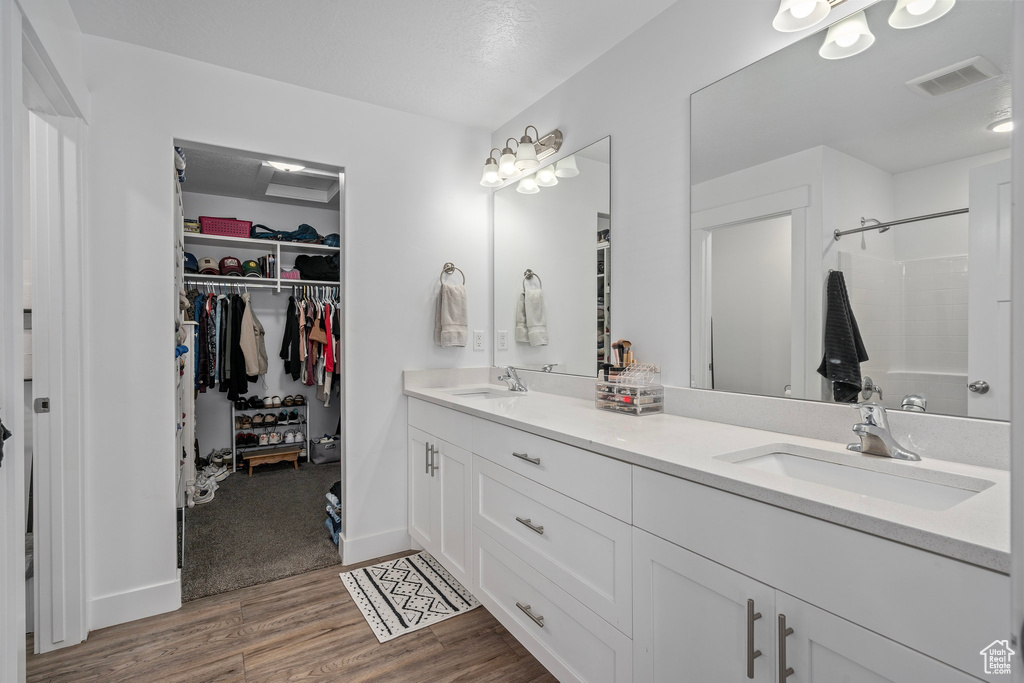 Bathroom featuring wood finished floors, a shower, a spacious closet, and double vanity