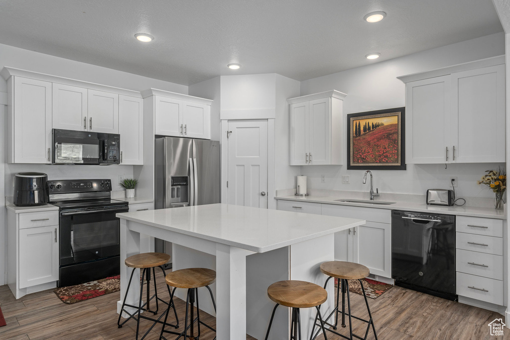 Kitchen featuring black appliances, a sink, a kitchen bar, wood finished floors, and recessed lighting