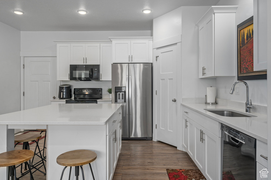 Kitchen with black appliances, a sink, a kitchen bar, white cabinetry, and recessed lighting