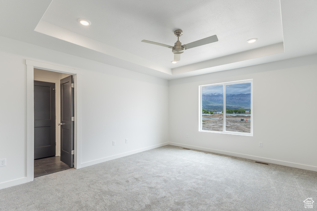 Carpeted spare room with a tray ceiling, ceiling fan, baseboards, and recessed lighting
