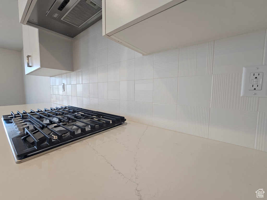 Kitchen with ventilation hood, backsplash, white cabinetry, light stone countertops, and stainless steel gas cooktop