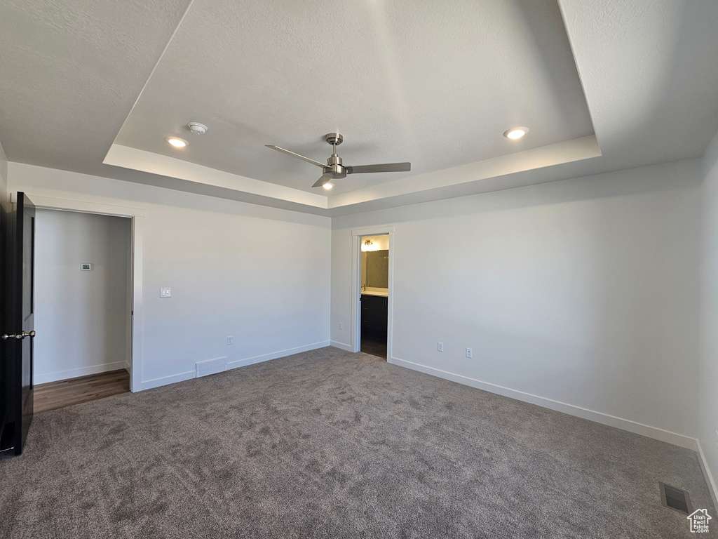 Unfurnished bedroom with a tray ceiling, carpet flooring, baseboards, recessed lighting, and ceiling fan