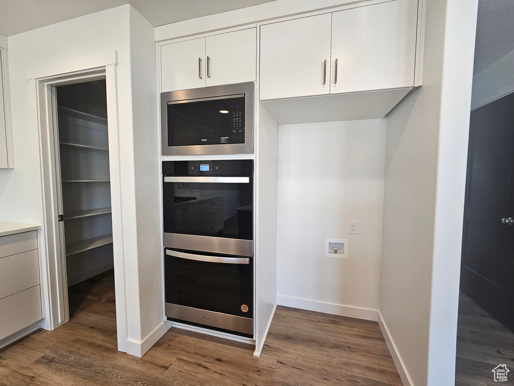 Kitchen featuring appliances with stainless steel finishes, dark wood-style flooring, white cabinetry, baseboards, and light countertops