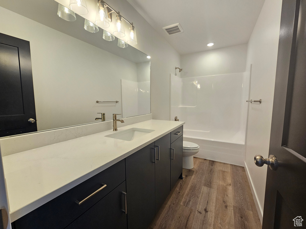 Bathroom with wood finished floors, toilet, vanity, shower / washtub combination, and recessed lighting