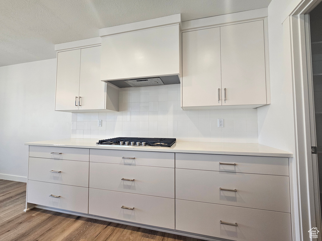 Kitchen with wood finished floors, decorative backsplash, light countertops, custom exhaust hood, and stainless steel gas cooktop