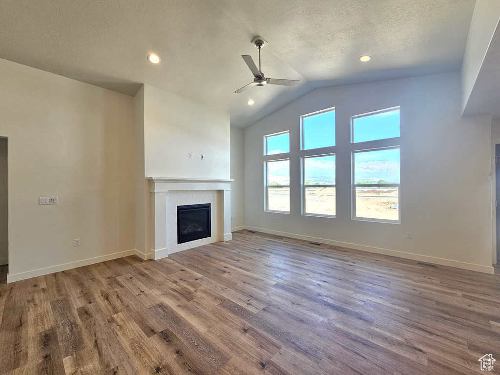Unfurnished living room featuring a ceiling fan, a glass covered fireplace, lofted ceiling, wood finished floors, and a textured ceiling
