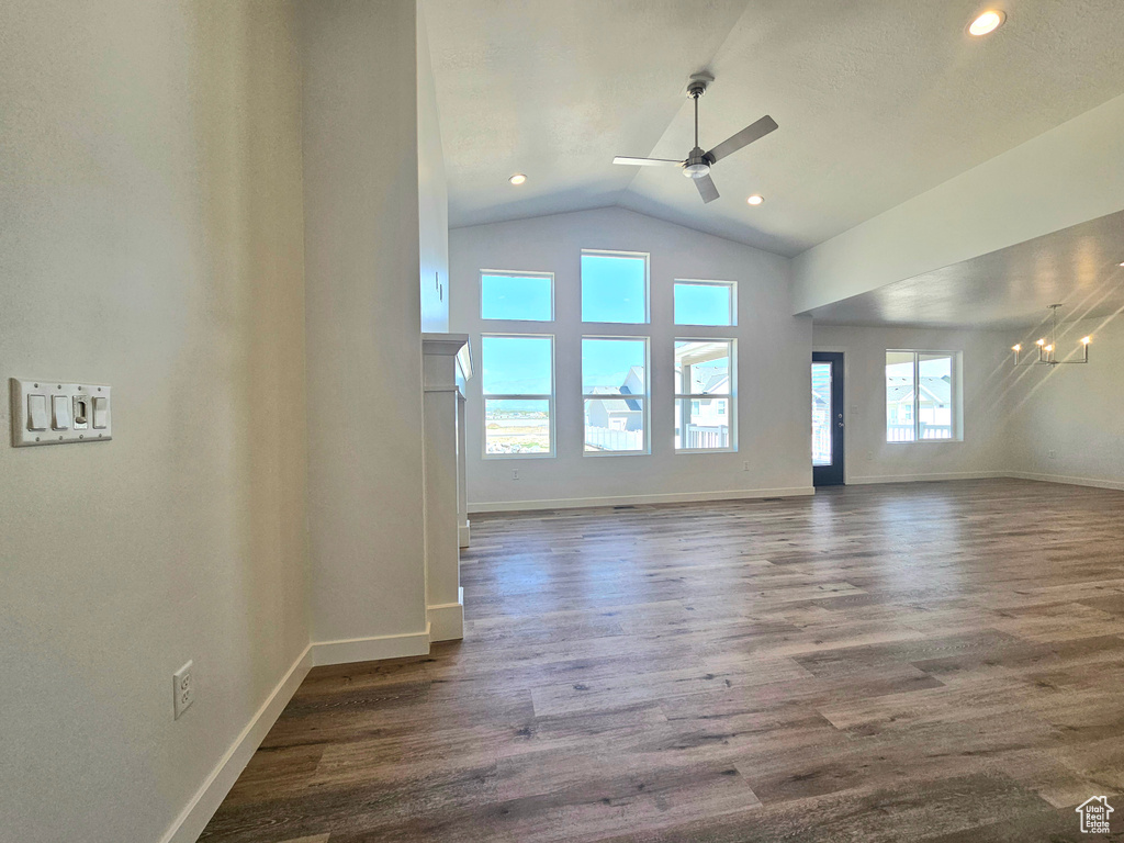 Unfurnished living room with a ceiling fan, dark wood-type flooring, baseboards, a chandelier, and high vaulted ceiling