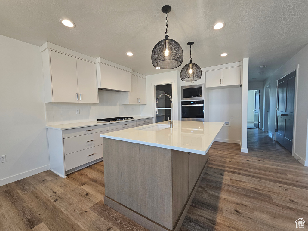 Kitchen featuring stainless steel oven, gas cooktop, wood finished floors, white cabinets, and baseboards