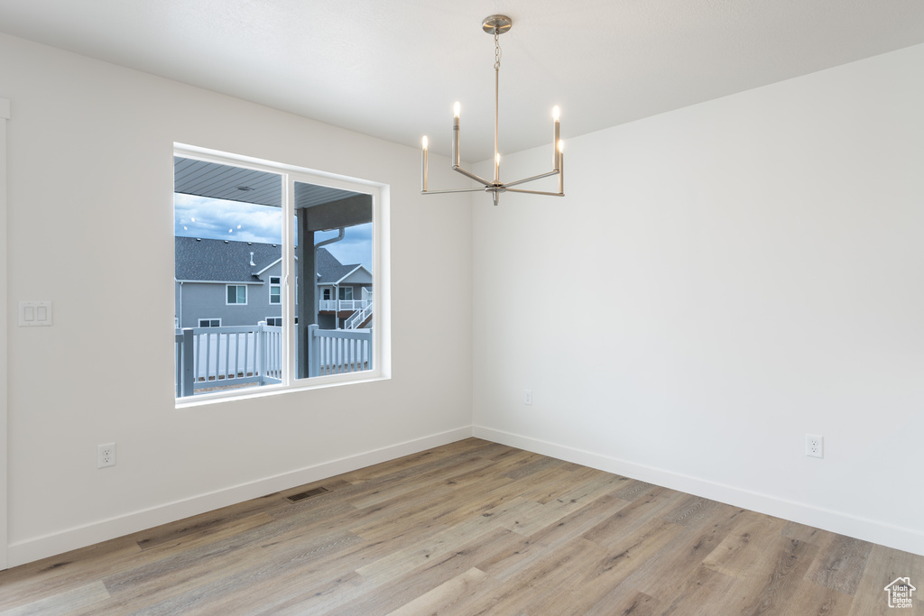 Spare room with a chandelier, light wood-style flooring, and baseboards