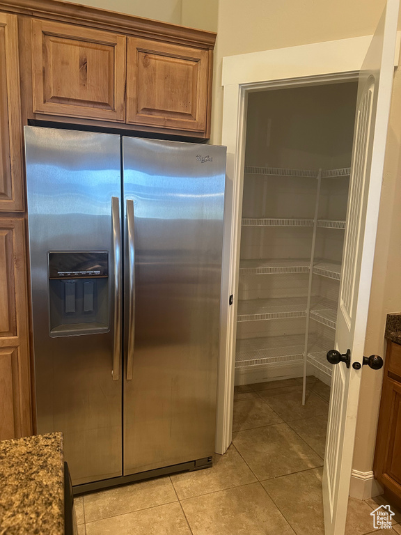 Kitchen with stainless steel fridge with ice dispenser, brown cabinets, light tile patterned floors, and dark stone counters